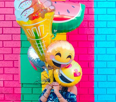 Mujer cubre su rostro con varios globos con un fondo colorido en Marca digital