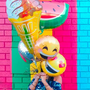 Mujer cubre su rostro con varios globos con un fondo colorido en Marca digital