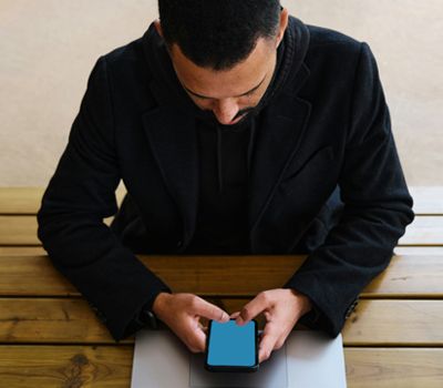 Hombre frente a su Laptop con su celular revisando proceso de creación de marca digital