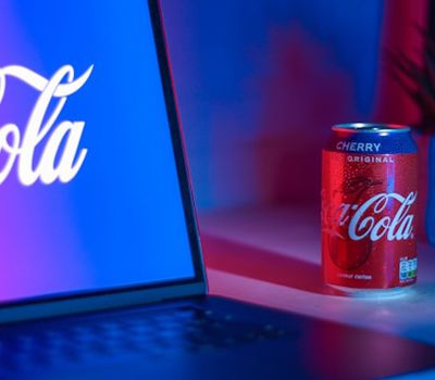 Una lata de Coca Cola junto a una laptop con una imagen de un logo de la marca que representa revolución de marketing de marca