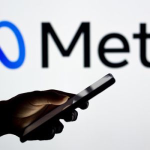 Plano cerrado de mano utilizando celular y de fondo la marca meta como ejemplo de identidad gráfica para empresas tecnológicas